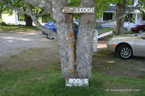 Fig. #89.  This old sign has been replaced by a handsome new sign which still says "Roseledge Books" and "open 2-6 p.m." with an arrow pointing left.  But the tree is the same, across the road from the Sea Street street sign. 
